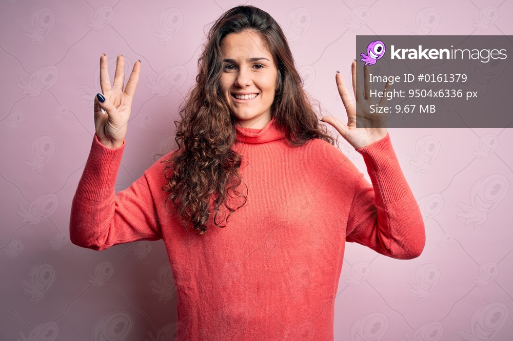 Young beautiful woman with curly hair wearing turtleneck sweater over pink background showing and pointing up with fingers number eight while smiling confident and happy.