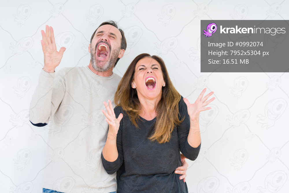 Beautiful middle age couple in love over isolated background celebrating mad and crazy for success with arms raised and closed eyes screaming excited. Winner concept