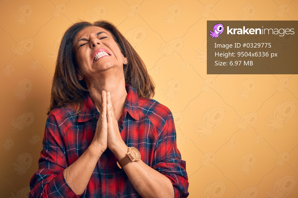 Middle age beautiful woman wearing casual shirt standing over isolated yellow background begging and praying with hands together with hope expression on face very emotional and worried. Begging.