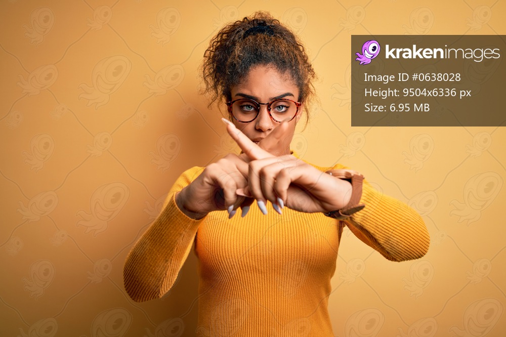 Young beautiful african american girl wearing sweater and glasses over yellow background Rejection expression crossing fingers doing negative sign