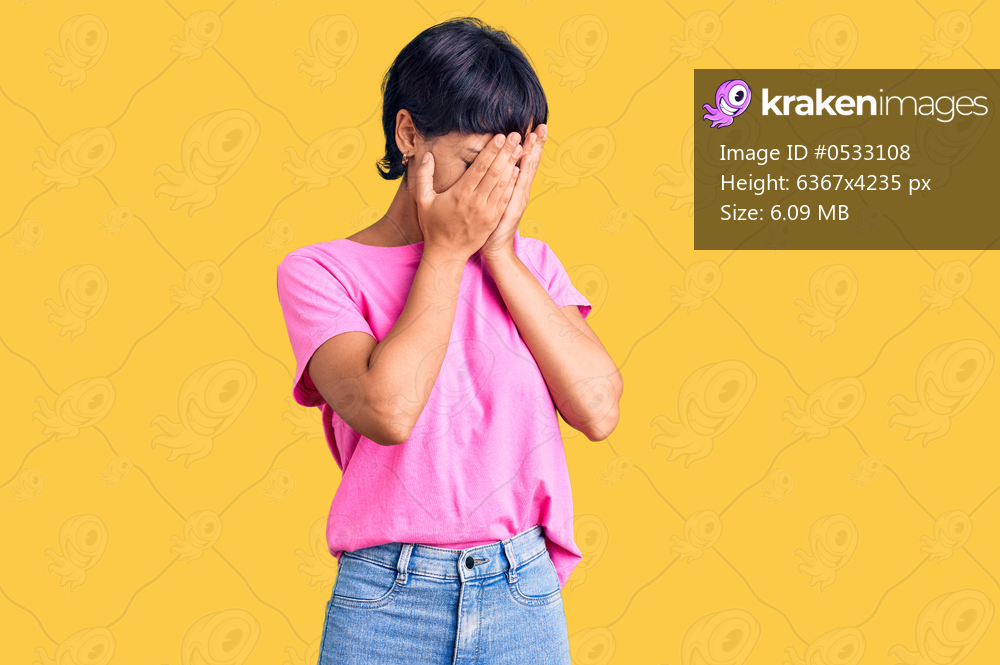 Young brunette woman with short hair wearing casual clothes with sad expression covering face with hands while crying. depression concept. 