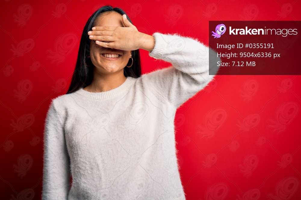 Young beautiful asian woman wearing casual sweater and glasses over red background smiling and laughing with hand on face covering eyes for surprise. Blind concept.