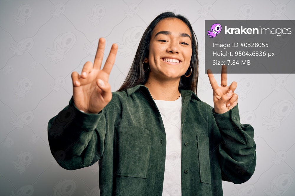 Young beautiful asian woman wearing casual shirt standing over isolated white background smiling looking to the camera showing fingers doing victory sign. Number two.