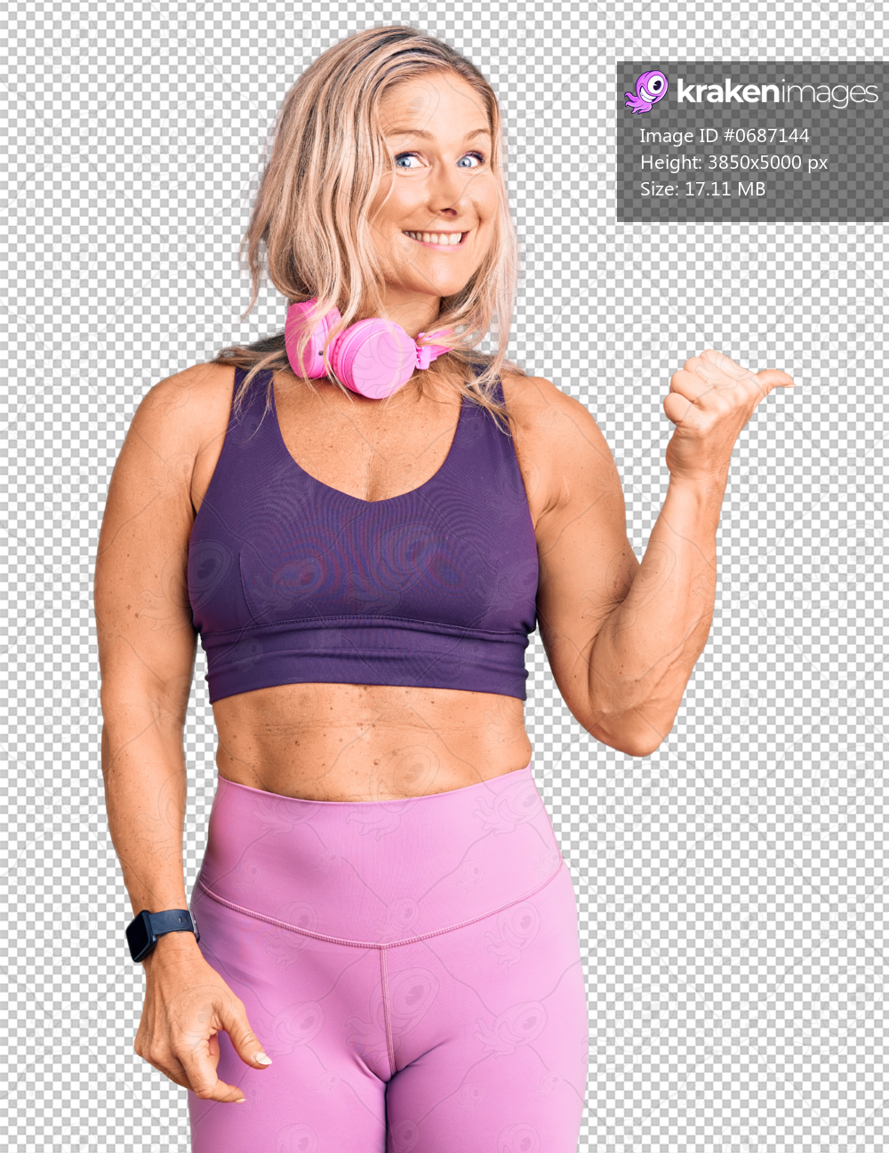 Middle age fit blonde woman wearing gym clothes and using headphones smiling with happy face looking and pointing to the side with thumb up.