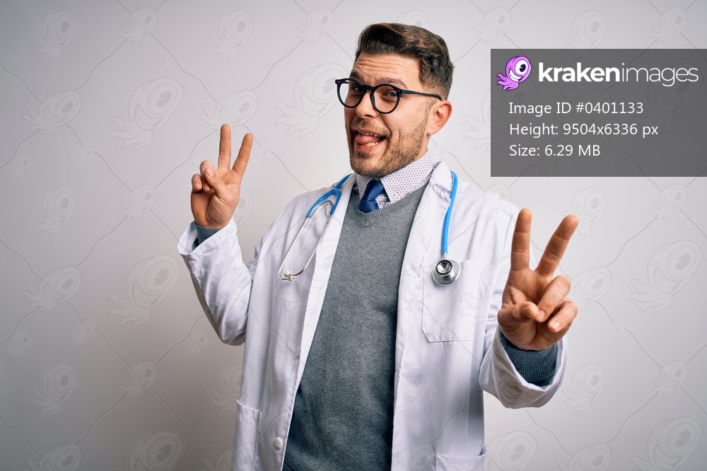 Young doctor man with blue eyes wearing medical coat and stethoscope over isolated background smiling with tongue out showing fingers of both hands doing victory sign. Number two.