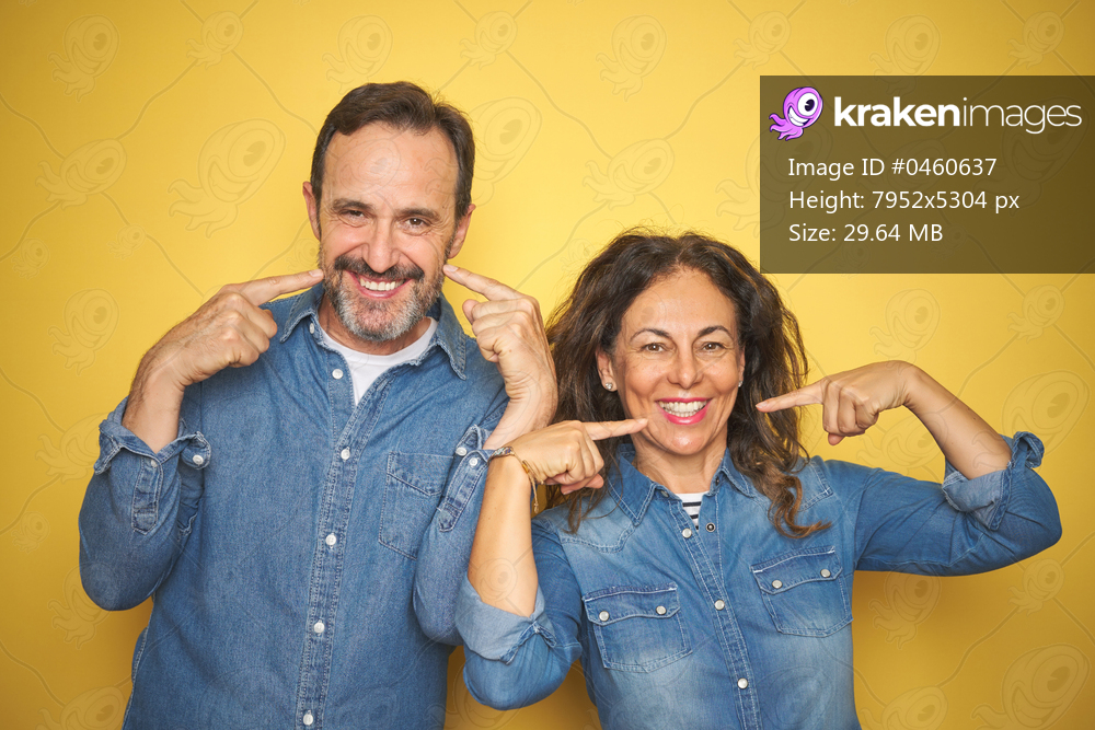 Beautiful middle age couple together standing over isolated yellow background smiling cheerful showing and pointing with fingers teeth and mouth. Dental health concept.
