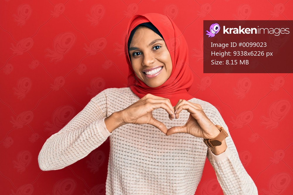 Young african american woman wearing traditional islamic hijab scarf smiling in love doing heart symbol shape with hands. romantic concept. 