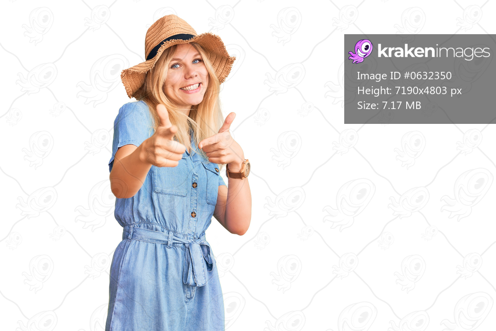 Young beautiful blonde woman wearing summer hat and dress pointing fingers to camera with happy and funny face. good energy and vibes. 