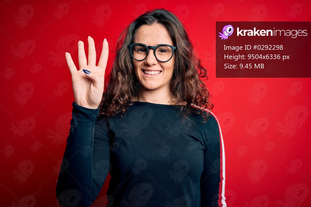 Young beautiful woman with curly hair wearing sweater and glasses over red background showing and pointing up with fingers number four while smiling confident and happy.