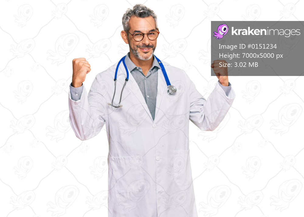 Middle age grey-haired man wearing doctor uniform and stethoscope screaming proud, celebrating victory and success very excited with raised arms 