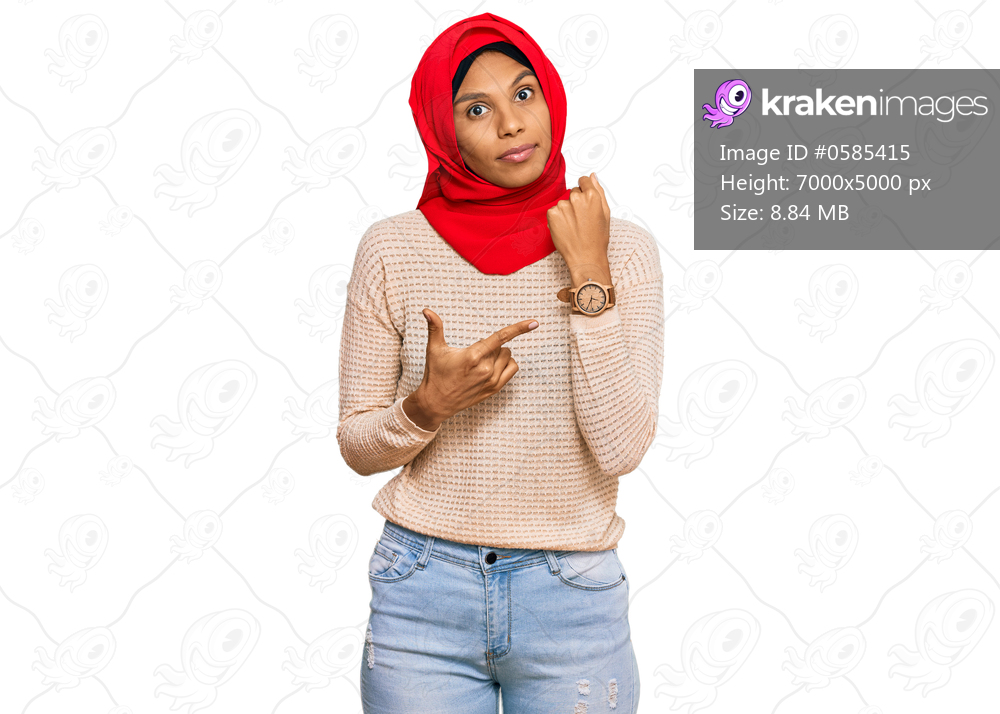 Young african american woman wearing traditional islamic hijab scarf in hurry pointing to watch time, impatience, looking at the camera with relaxed expression 