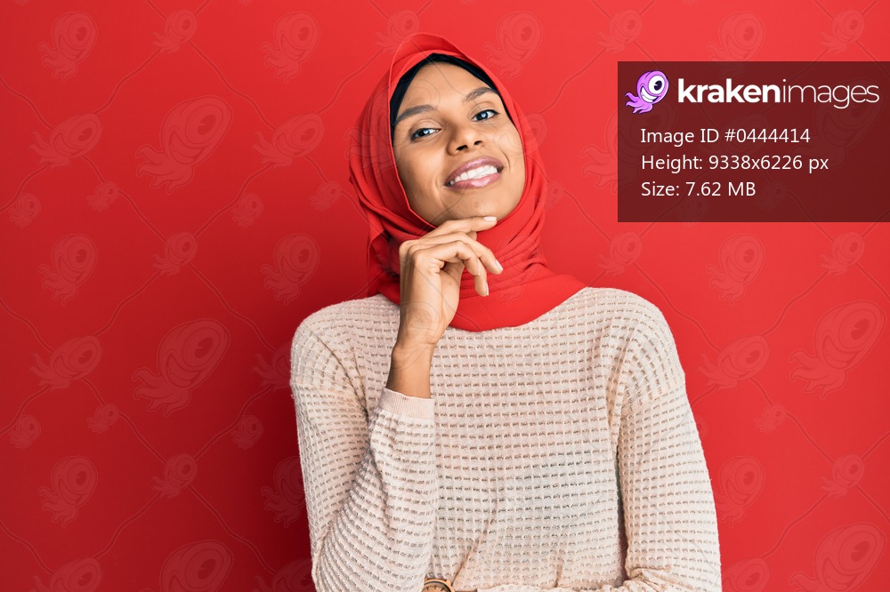 Young african american woman wearing traditional islamic hijab scarf smiling looking confident at the camera with crossed arms and hand on chin. thinking positive. 
