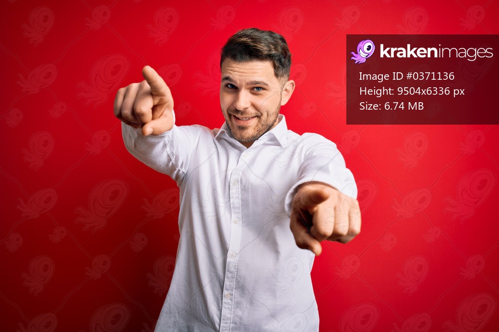 Young business man with blue eyes wearing elegant shirt standing over red isolated background pointing to you and the camera with fingers, smiling positive and cheerful