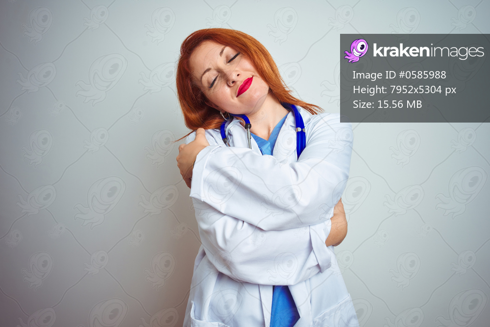 Young redhead doctor woman using stethoscope over white isolated background Hugging oneself happy and positive, smiling confident. Self love and self care