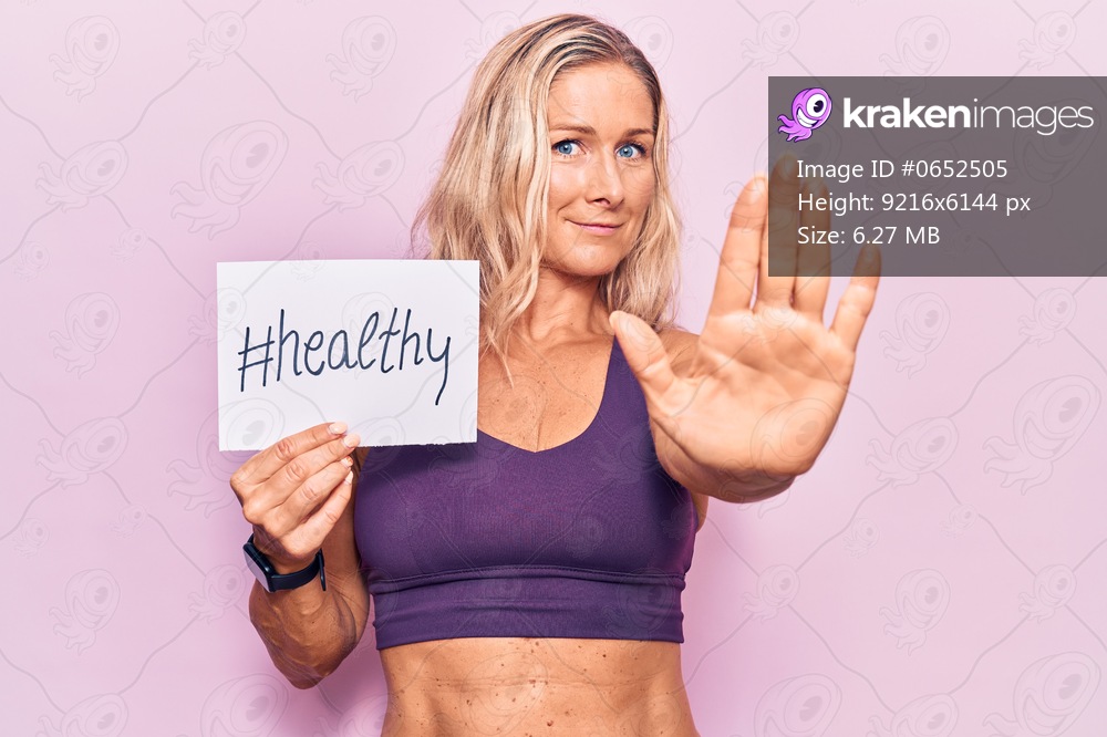 Middle age caucasian blonde woman wearing sportswear holding healthy banner with open hand doing stop sign with serious and confident expression, defense gesture 