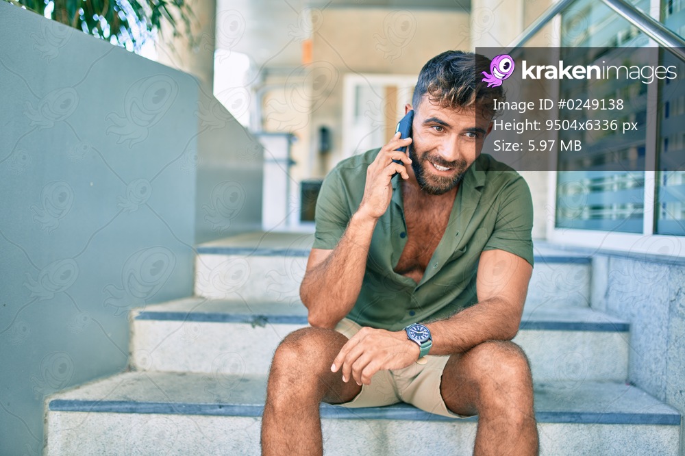 Young hispanic man smiling happy using smartphone sitting on stairs