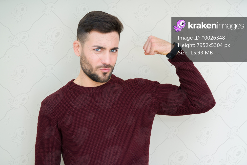Young handsome man wearing a sweater over isolated background Strong person showing arm muscle, confident and proud of power