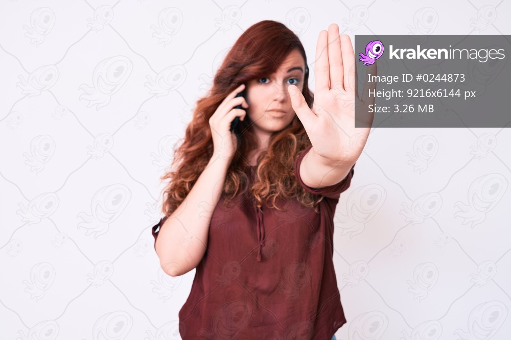 Young beautiful woman having conversation talking on the smartphone with open hand doing stop sign with serious and confident expression, defense gesture 