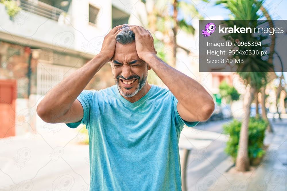Middle age grey-haired man wearing casual clothes at street of city suffering from headache desperate and stressed because pain and migraine. hands on head. 