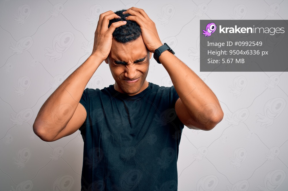 Young handsome african american man wearing casual t-shirt standing over white background suffering from headache desperate and stressed because pain and migraine. Hands on head.