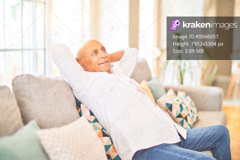 Senior handsome man smiling happy and confident. Sitting on the sofa relaxed at home