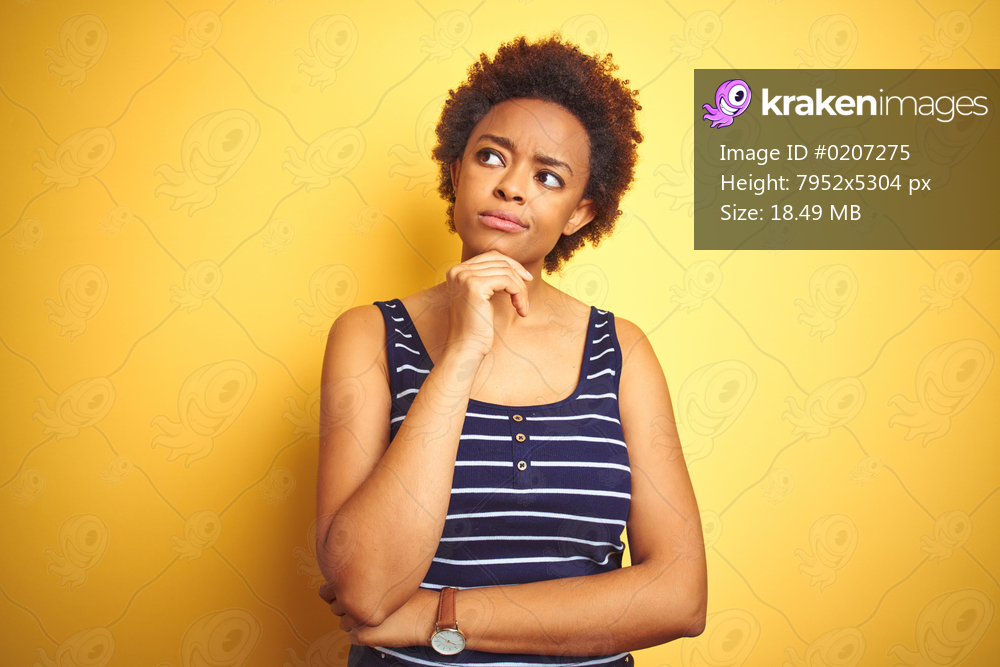 Beauitul african american woman wearing summer t-shirt over isolated yellow background with hand on chin thinking about question, pensive expression. Smiling with thoughtful face. Doubt concept.