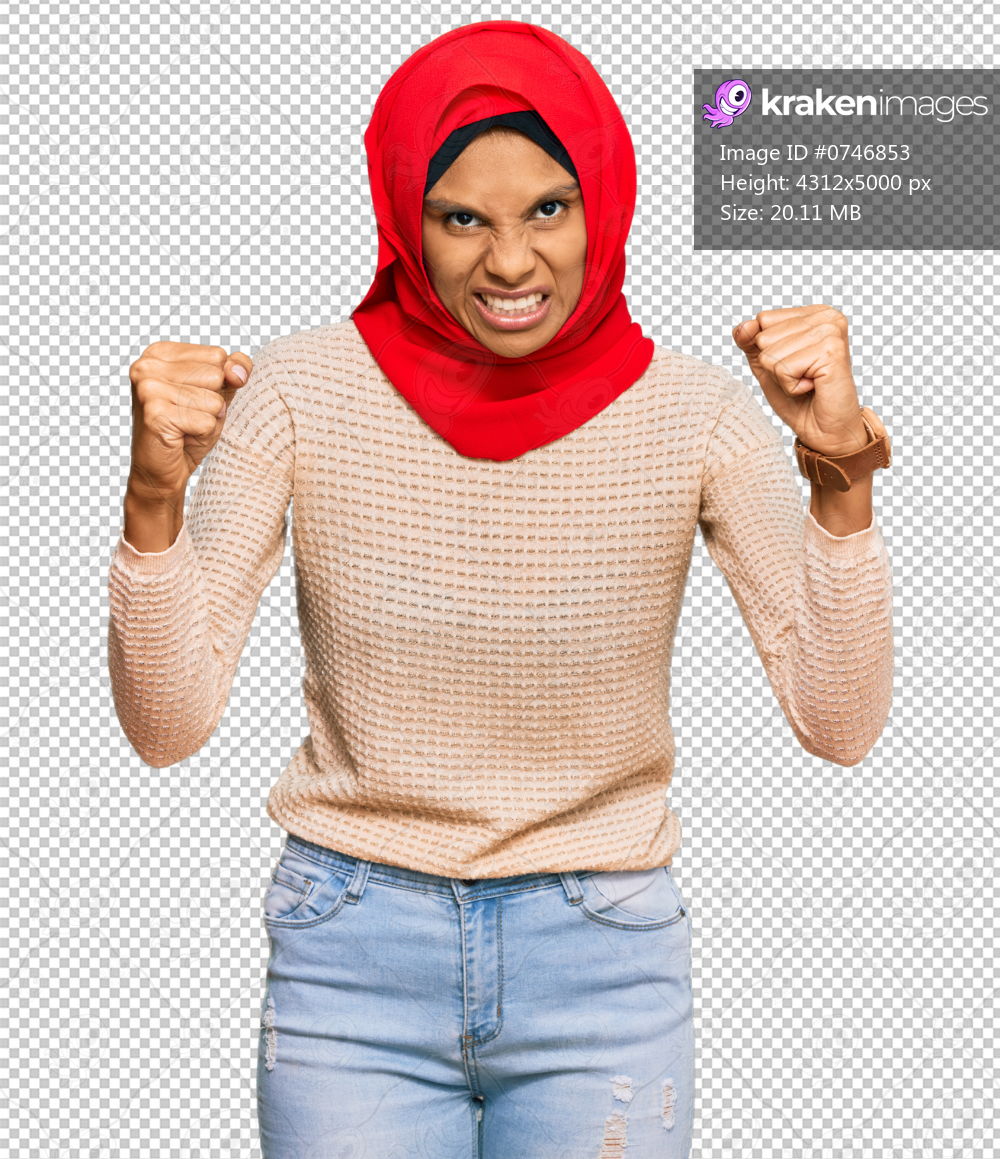 Young african american woman wearing traditional islamic hijab scarf angry and mad raising fists frustrated and furious while shouting with anger. rage and aggressive concept.