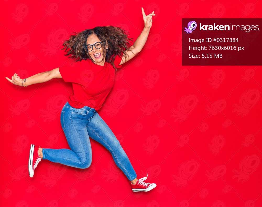 Middle age beautiful hispanic woman wearing casual clothes and glasses smiling happy. Jumping with smile on face over isolated red background