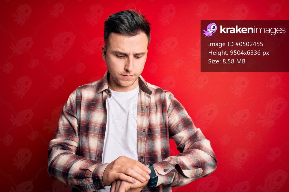 Young handsome caucasian man wearing casual modern shirt over red isolated background Checking the time on wrist watch, relaxed and confident
