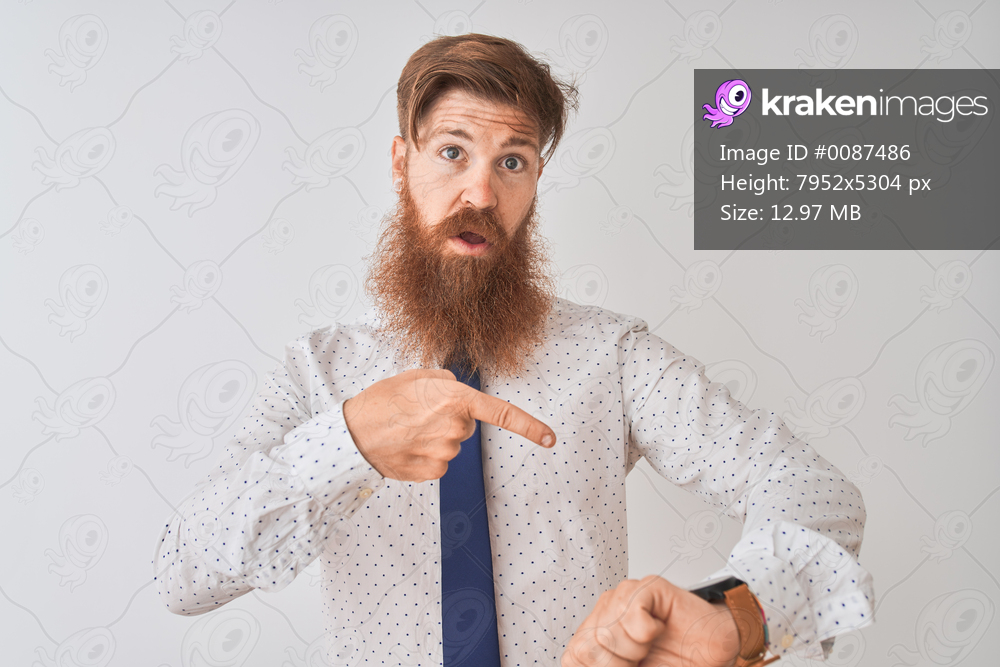 Young redhead irish businessman standing over isolated white background In hurry pointing to watch time, impatience, upset and angry for deadline delay