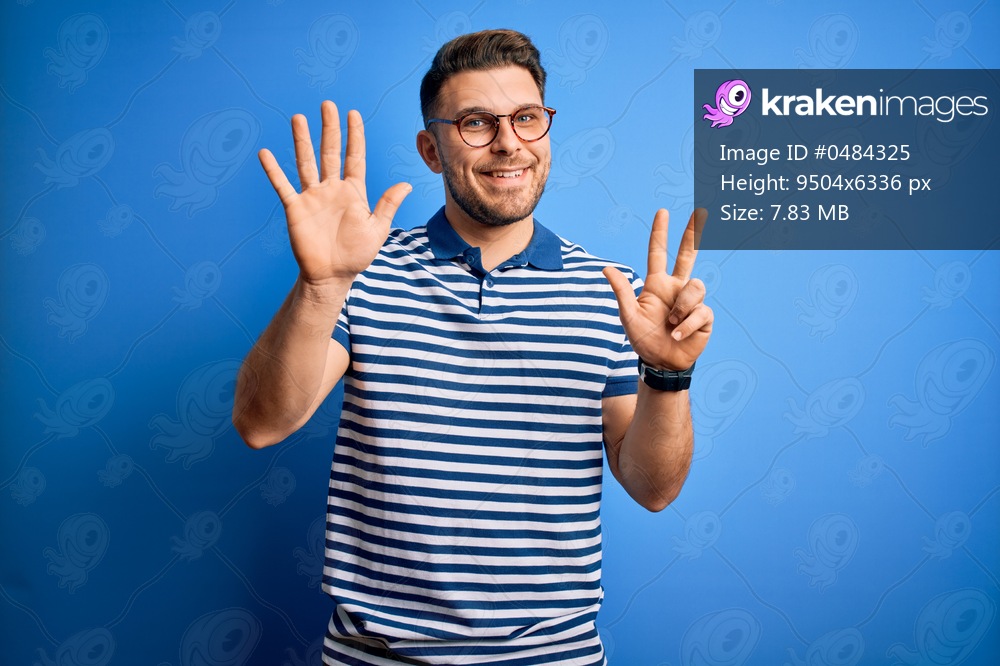 Young man with blue eyes wearing glasses and casual striped t-shirt over blue background showing and pointing up with fingers number eight while smiling confident and happy.