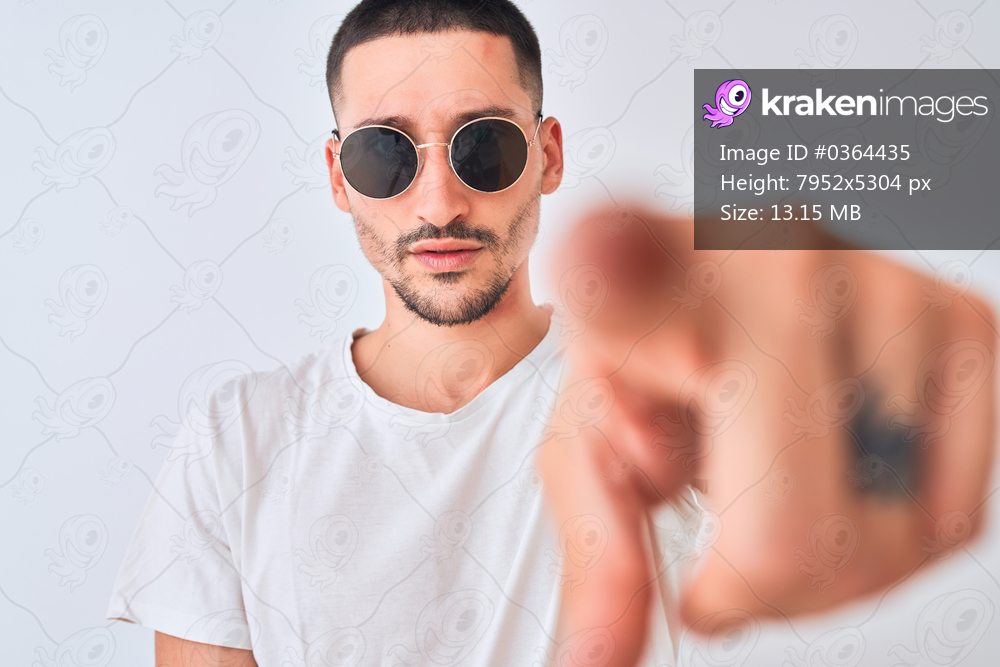 Young handsome man wearing sunglasses and casual t-shirt over isolated background pointing with finger to the camera and to you, hand sign, positive and confident gesture from the front