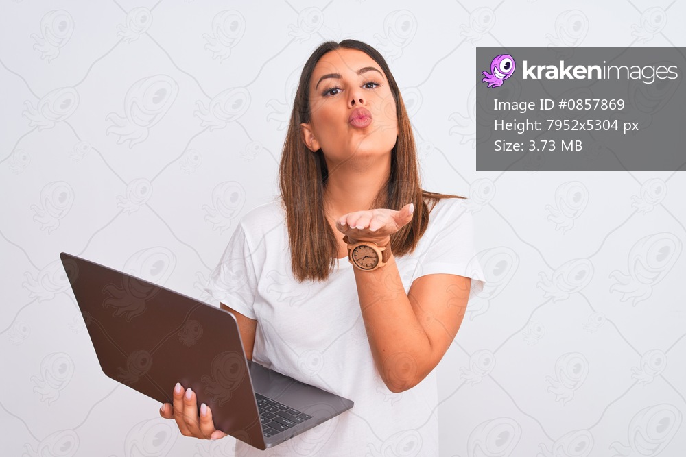 Beautiful young woman working using computer laptop over white background looking at the camera blowing a kiss with hand on air being lovely and sexy. Love expression.