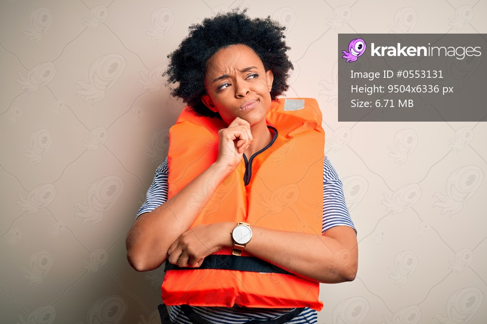Young African American afro woman with curly hair wearing orange protection lifejacket with hand on chin thinking about question, pensive expression. Smiling with thoughtful face. Doubt concept.