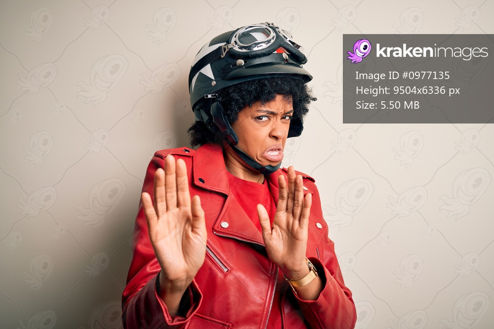 Young African American afro motorcyclist woman with curly hair wearing motorcycle helmet disgusted expression, displeased and fearful doing disgust face because aversion reaction. With hands raised