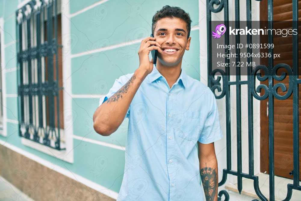 Young latin man smiling happy using smartphone walking at the city.