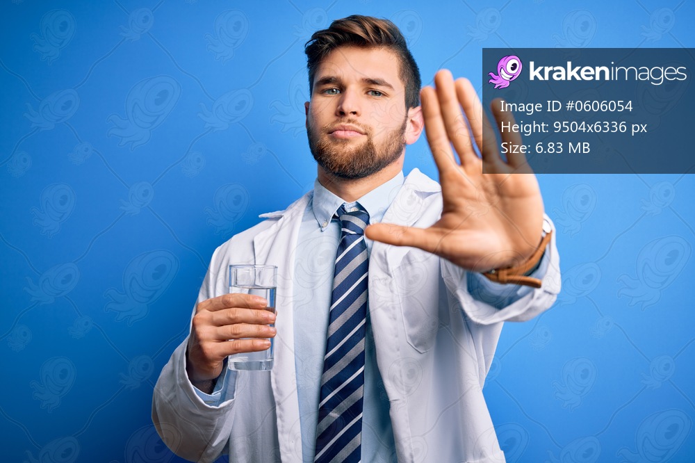 Young blond doctor man with beard and blue eyes wearing coat and tie drinking glass of water with open hand doing stop sign with serious and confident expression, defense gesture