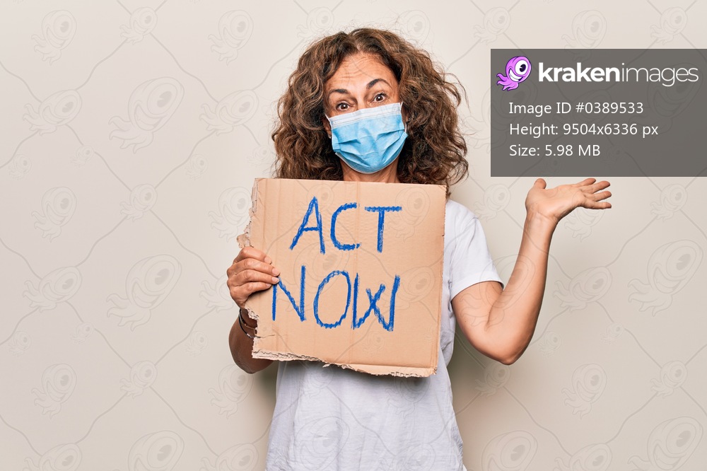Middle age woman wearing coronavirus protection mask holding act now protest cardboard celebrating achievement with happy smile and winner expression with raised hand