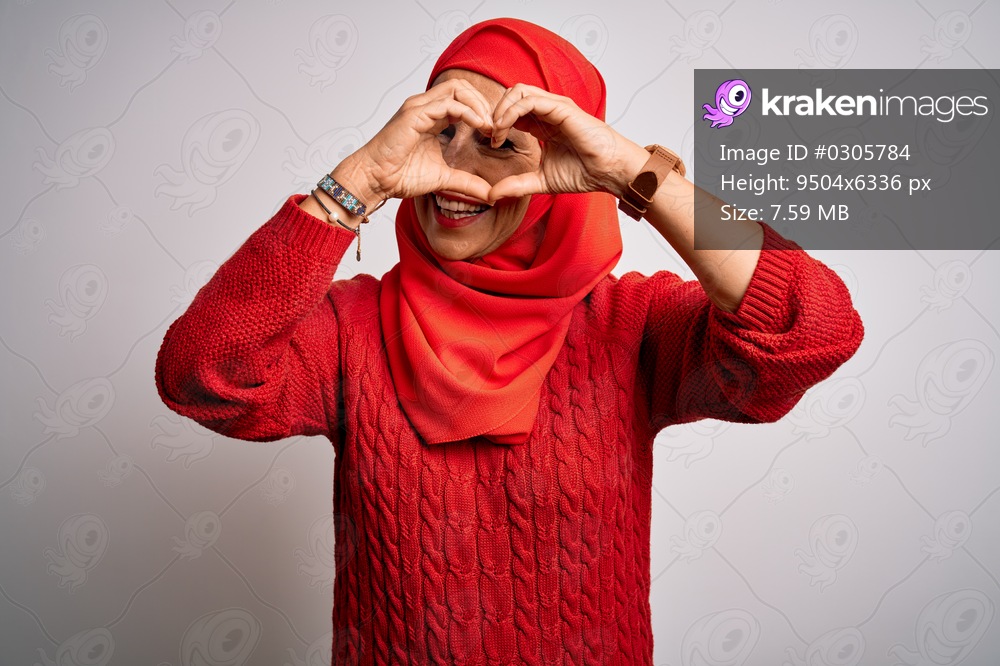 Middle age brunette woman wearing muslim traditional hijab over isolated white background Doing heart shape with hand and fingers smiling looking through sign