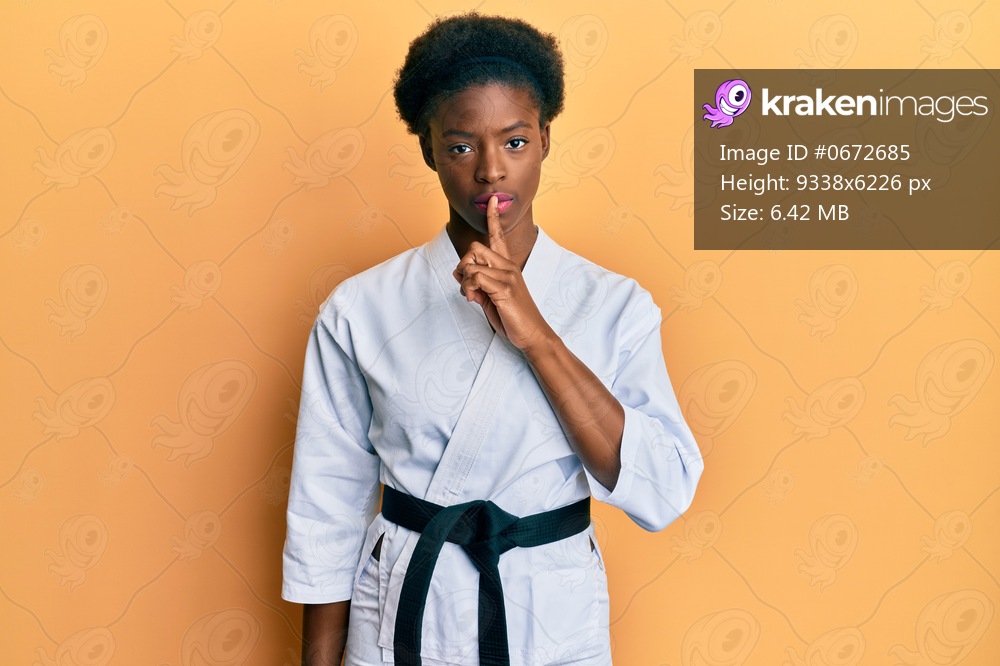 Young african american girl wearing karate kimono and black belt asking to be quiet with finger on lips. silence and secret concept. 