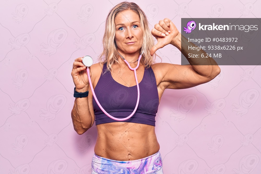 Middle age caucasian blonde woman wearing sport clothes holding stethoscope with angry face, negative sign showing dislike with thumbs down, rejection concept 