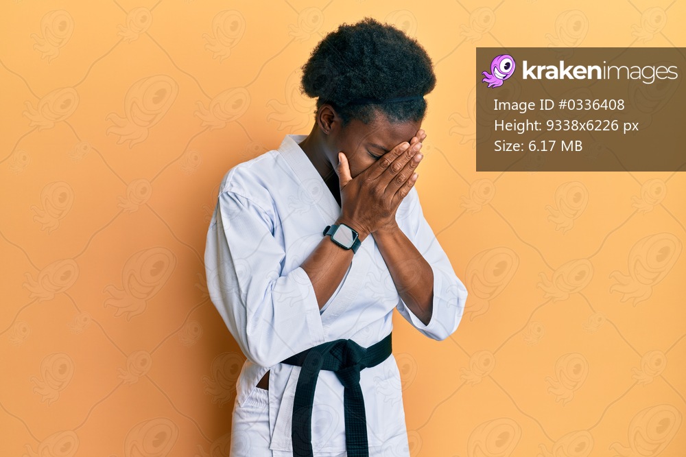 Young african american girl wearing karate kimono and black belt with sad expression covering face with hands while crying. depression concept. 