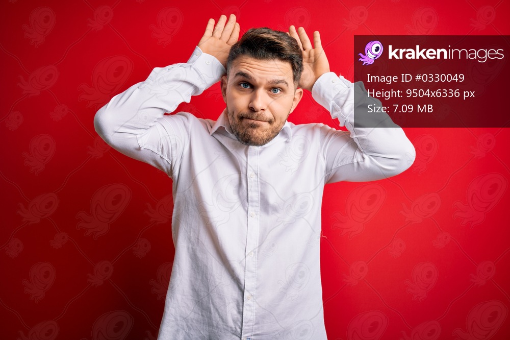 Young business man with blue eyes wearing elegant shirt standing over red isolated background Doing bunny ears gesture with hands palms looking cynical and skeptical. Easter rabbit concept.