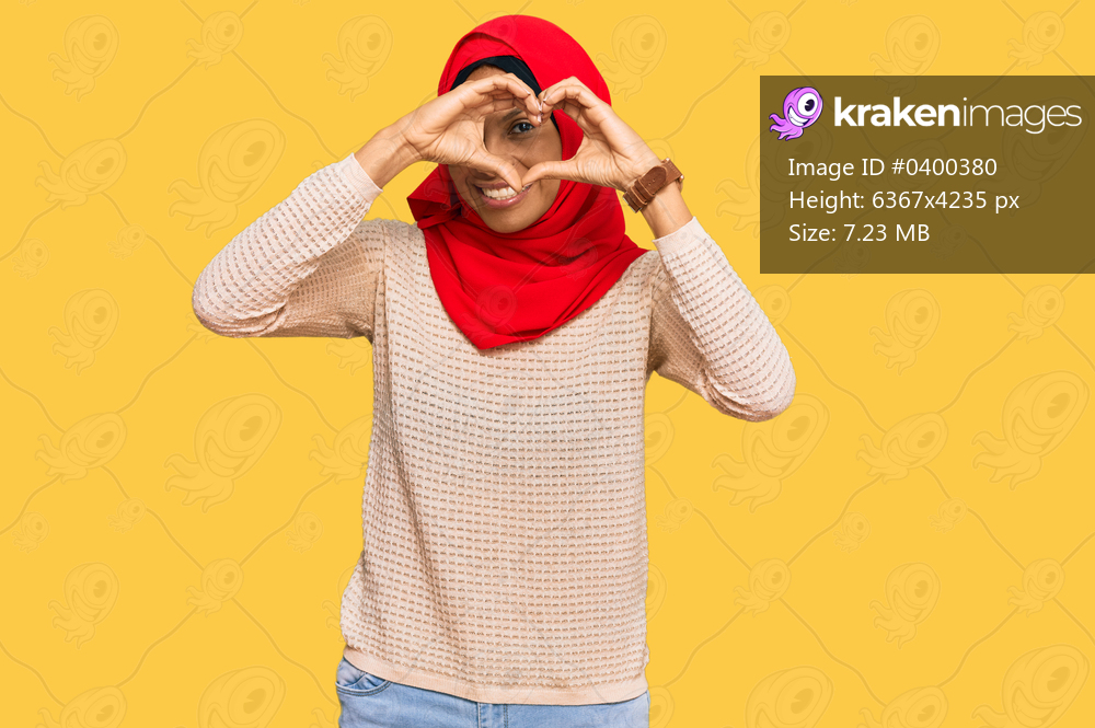 Young african american woman wearing traditional islamic hijab scarf doing heart shape with hand and fingers smiling looking through sign 