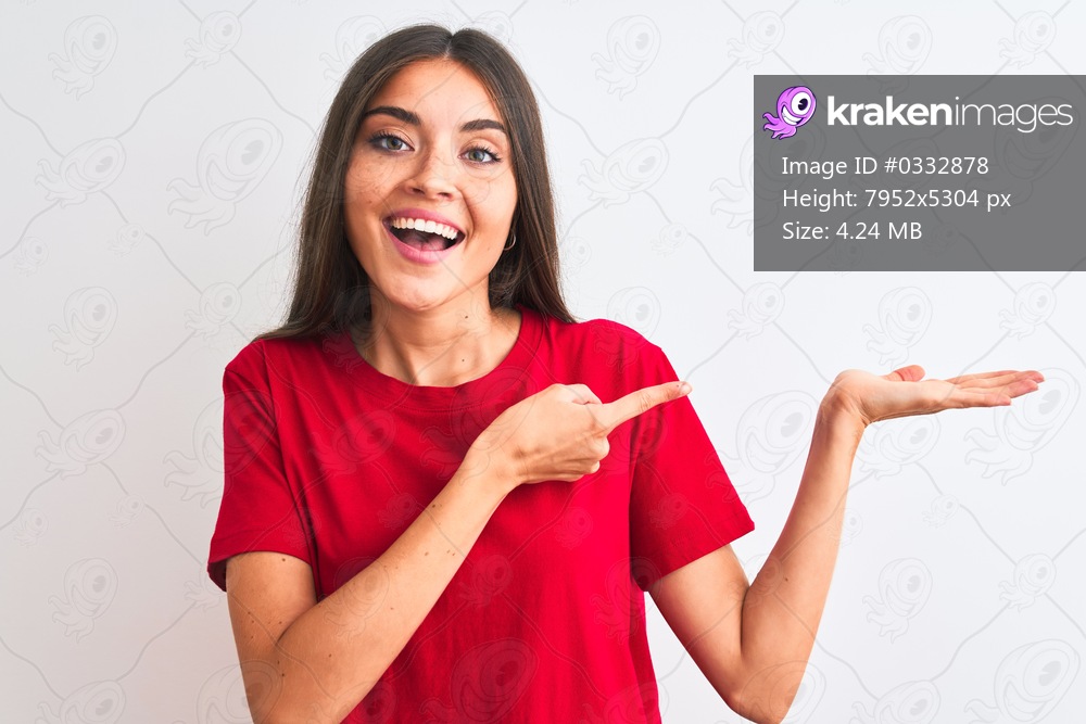 Young beautiful woman wearing red casual t-shirt standing over isolated white background amazed and smiling to the camera while presenting with hand and pointing with finger.