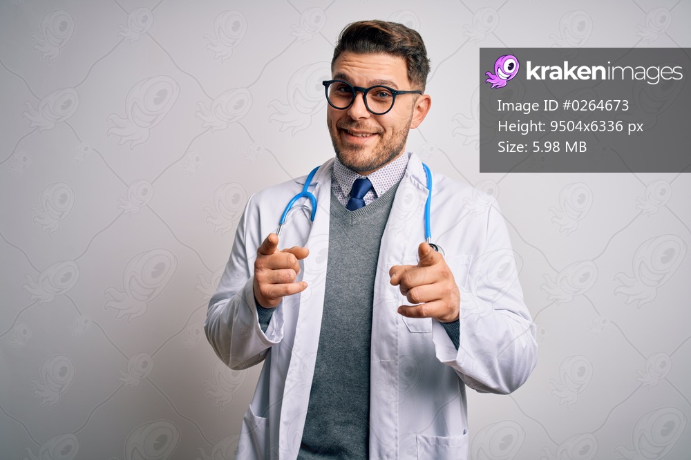 Young doctor man with blue eyes wearing medical coat and stethoscope over isolated background pointing fingers to camera with happy and funny face. Good energy and vibes.