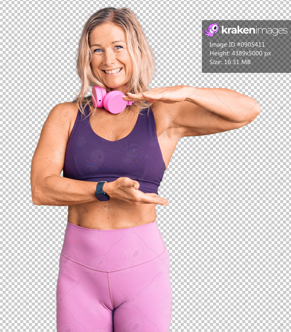 Middle age fit blonde woman wearing gym clothes and using headphones gesturing with hands showing big and large size sign, measure symbol. smiling looking at the camera. measuring concept.
