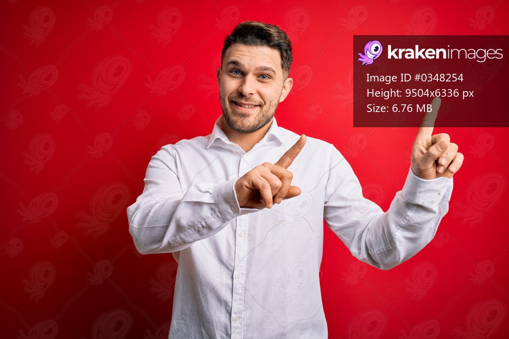 Young business man with blue eyes wearing elegant shirt standing over red isolated background smiling and looking at the camera pointing with two hands and fingers to the side.