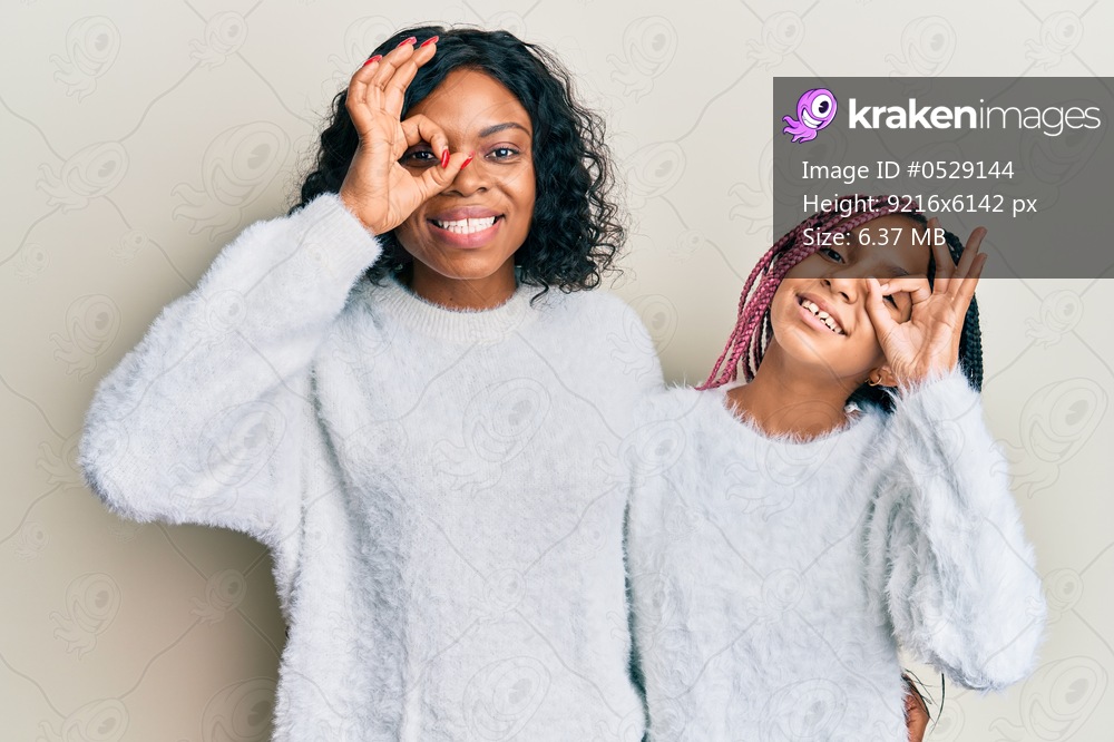 Beautiful african american mother and daughter wearing casual winter sweater doing ok gesture with hand smiling, eye looking through fingers with happy face. 