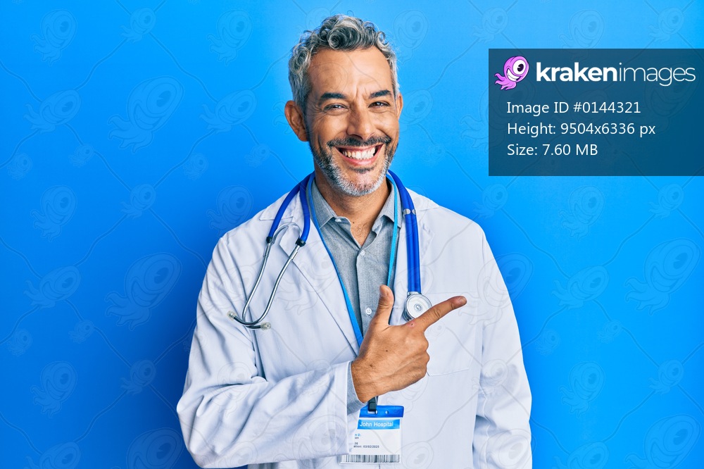 Middle age grey-haired man wearing doctor uniform and stethoscope cheerful with a smile of face pointing with hand and finger up to the side with happy and natural expression on face 